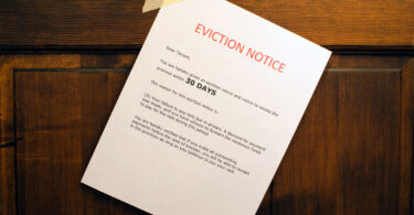 An eviction notice is posted on a wooden door informing a tenant to vacate the location in 30 days.