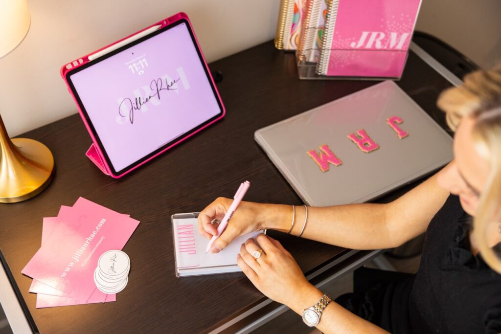 Jillian Rhae Maxwell sits at her desk with branded technology and stationery.