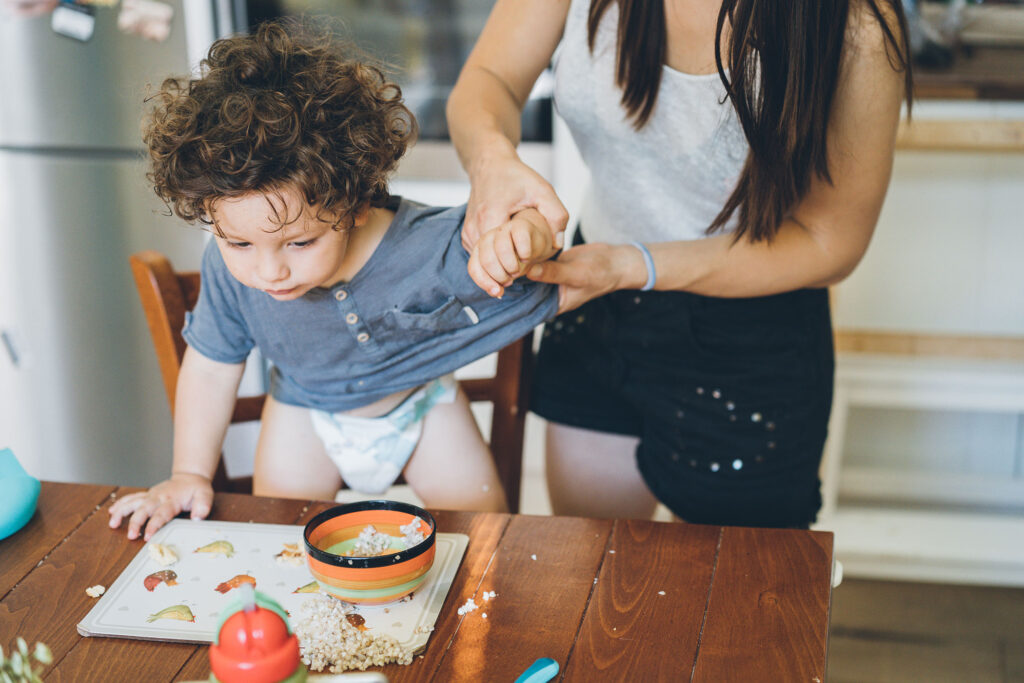 A mother cleans her toddler's hands after the child made a mess at meal time.