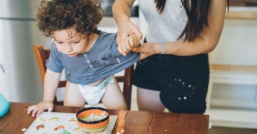 A mother cleans her toddler's hands after the child made a mess at meal time.