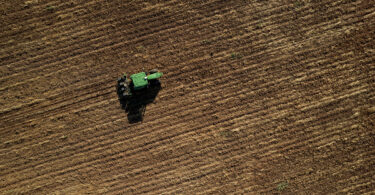 A green tractor drives down a brown-red dirt field.
