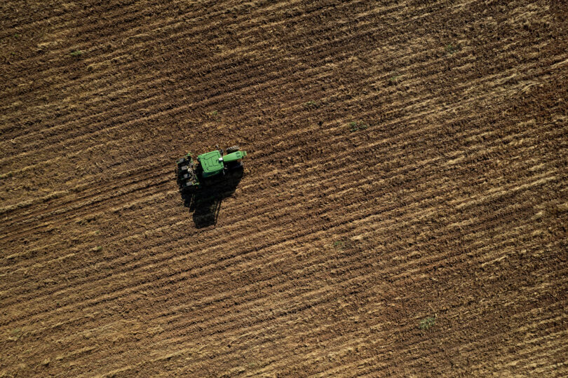 A green tractor drives down a brown-red dirt field.