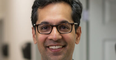 Portrait of UGA Rhodes scholar, Deep Shah, in a white doctor's coat, smiling