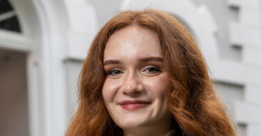 Portrait of UGA Rhodes scholar Natalie Navarrete. She is outdoors, smiling, in front of the entry arch of a stone building.