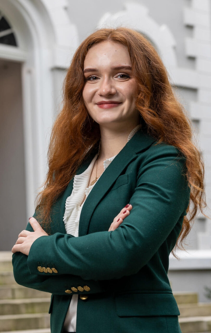 Portrait of UGA Rhodes scholar Natalie Navarrete. She is outdoors, smiling, in front of the entry arch of a stone building.