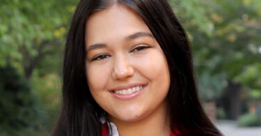 Portrait of 2024 UGA Rhodes Scholar Mariah Cady outdoors in a red sport-coat, smiling