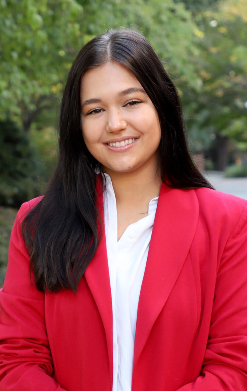 Portrait of 2024 UGA Rhodes Scholar Mariah Cady outdoors in a red sport-coat, smiling