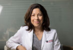 A female researcher in a UGA School of Medicine white lab coat smiles directly into the camera.