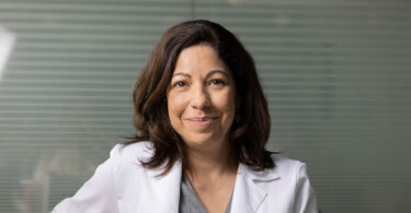 A female researcher in a UGA School of Medicine white lab coat smiles directly into the camera.