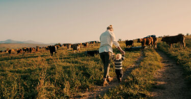 A woman walks on their family's farm with her small child.