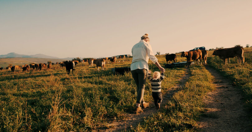 A woman walks on their family's farm with her small child.