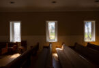 Rows of empty pews in a rural Georgia church are backlit from sun streaming in windows.