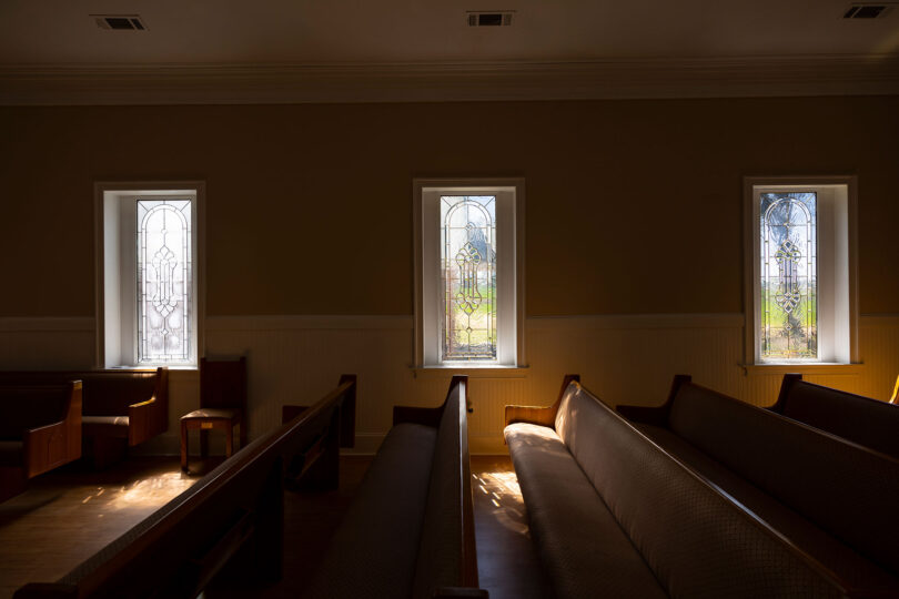 Rows of empty pews in a rural Georgia church are backlit from sun streaming in windows.