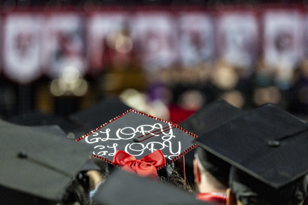 Detail of a decorated mortarboard that says "glory, glory" worn by a student during the 2023 Fall Graduate Commencement ceremony.