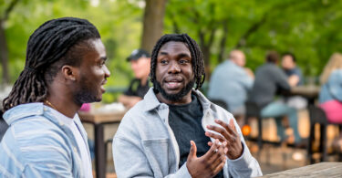 Two African American men have a conversation in a park.