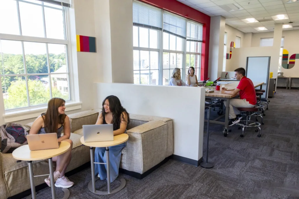 Students interact while sitting at small tables and desks in the Makerspace at the Creative Wing.