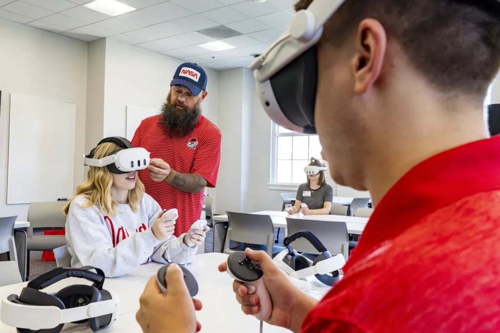 Graduate student Grace Chandler gets help with a VR headset from EITS associate Alvin Crews, while fellow student Dillon Cook tests an interactive game in the Creative Wing’s VR classroom at the Miller Learning Center