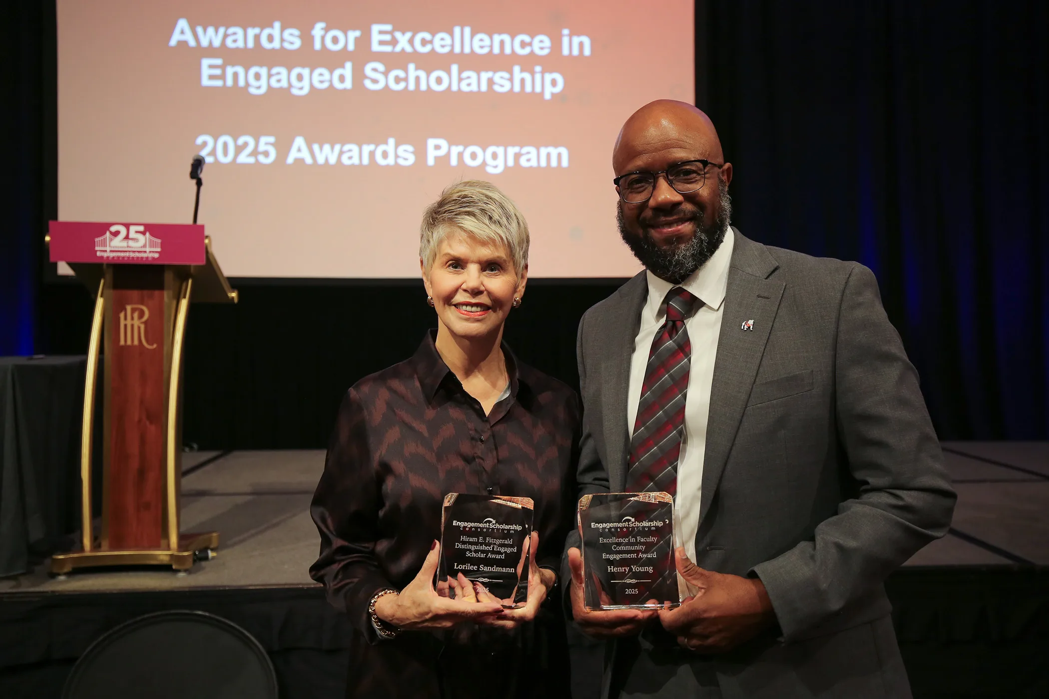 Lorilee Sandmann and Henry N. Young holding glass awards in front of a stage and podium.