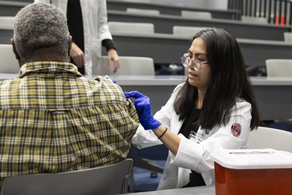 Nguyen Le administers a free flu shot to a community member during the Normaltown Community Health Fair at George Hall on the Health Sciences Campus.