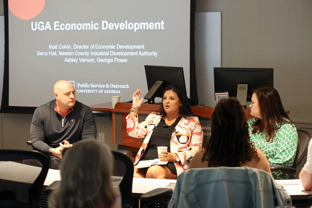 Three seated panelists deliver a presentation to a room full of UGA faculty.