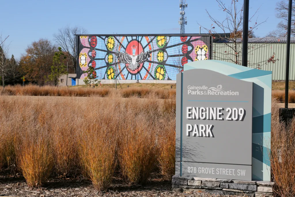 Gainesville Parks and Recreation sign for Engine 209 Park with colorful mural in background.