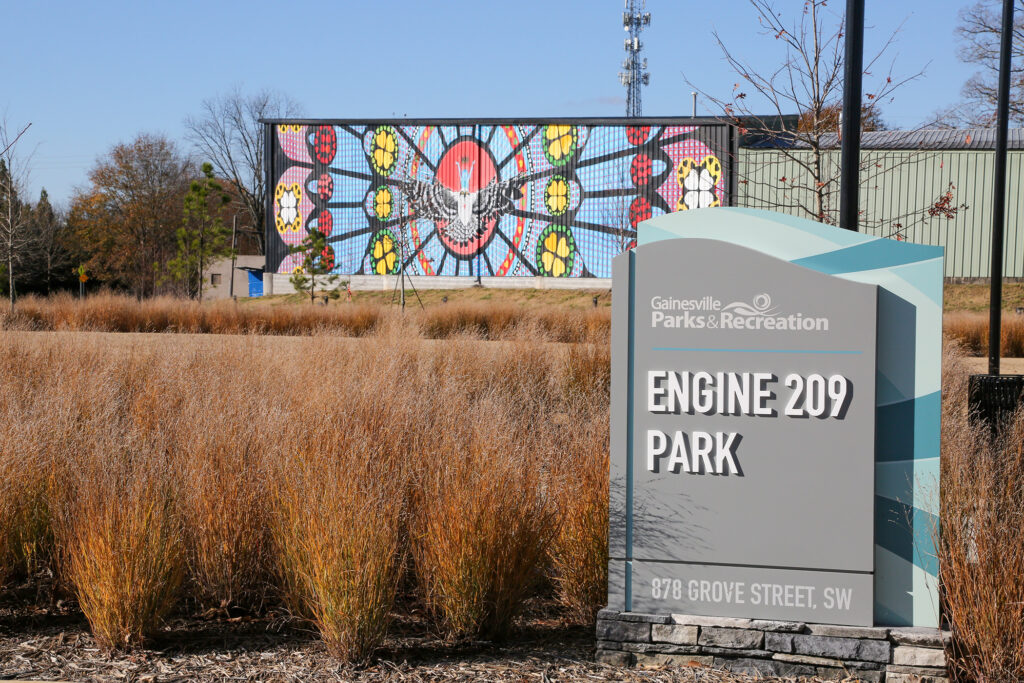 Gainesville Parks and Recreation sign for Engine 209 Park with colorful mural in background.