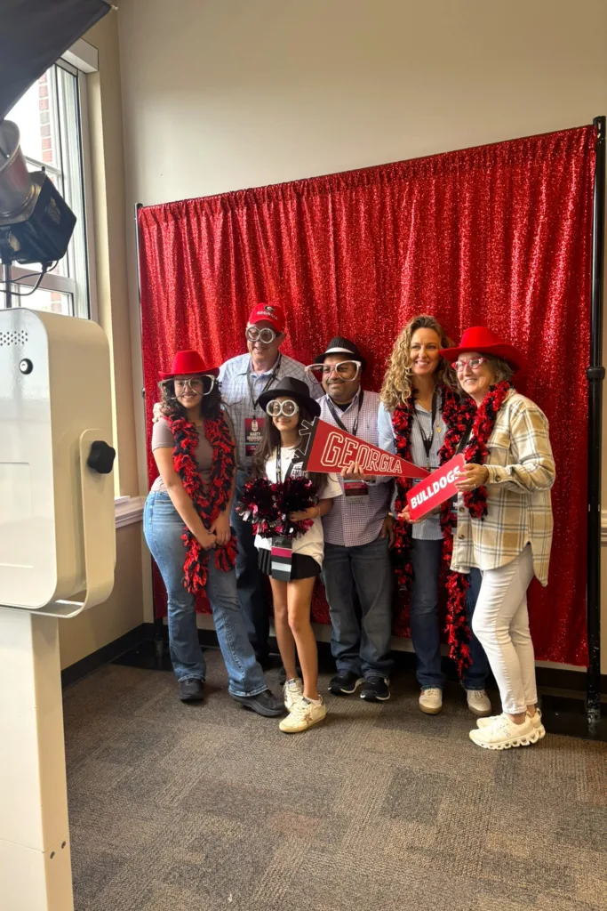 People dressed in red and black pose with University of Georgia props in front of a sparkly backdrop.