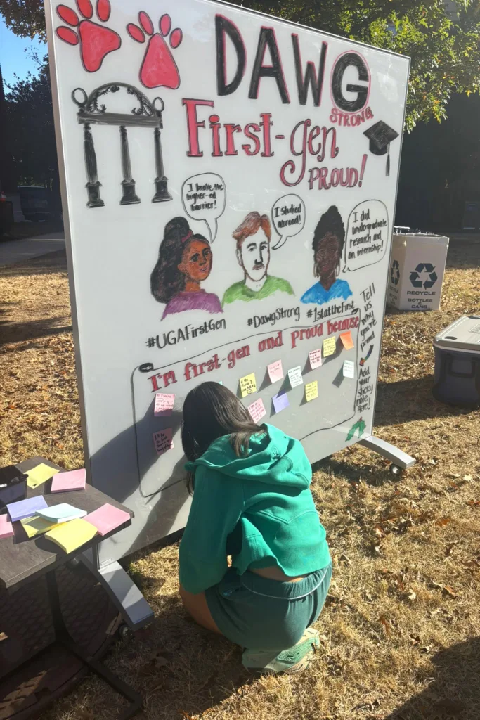 A student adds a note to a “Dawg Strong, First-Gen Proud” display filled with messages.
