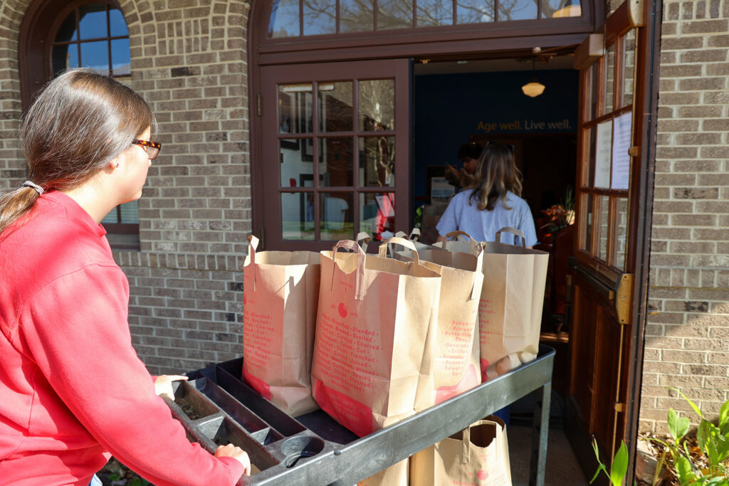 Students push cart of paper grocery bags into building for community food delivery.