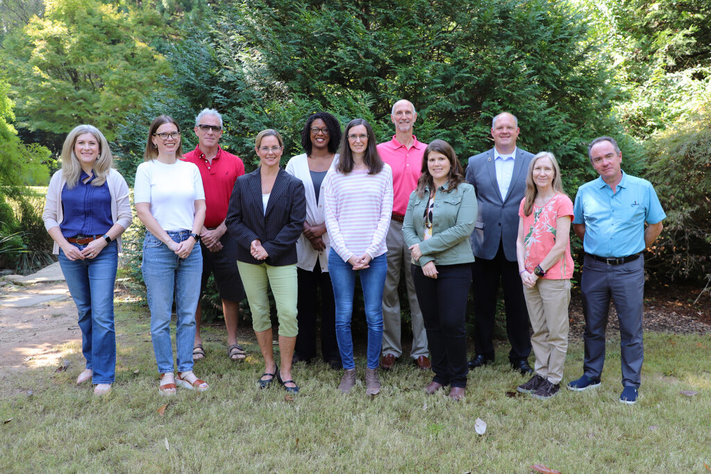 A group of 11 adults stands outside, facing the camera