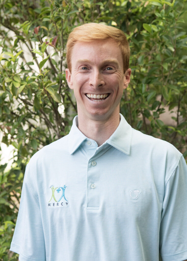 Headshot of a man standing outside in front of some foliage.