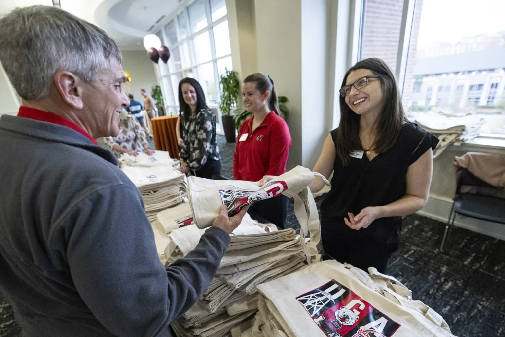 A woman hands a tote bag across a table to a man.