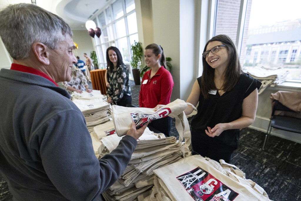 A woman hands a tote bag across a table to a man.