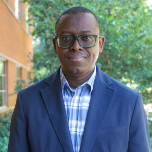 Environmental portrait of male researcher Nathaniel Hunsu outside in front of a tree.