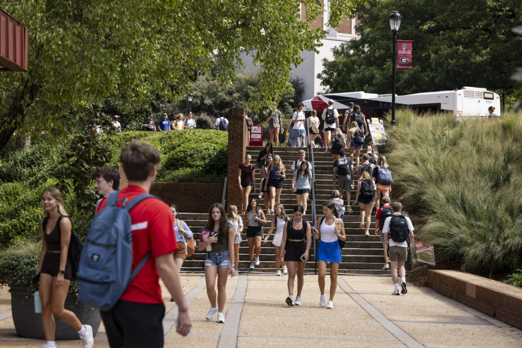 Students fill campus walkways and stairways, chatting and heading to class on a sunny day.