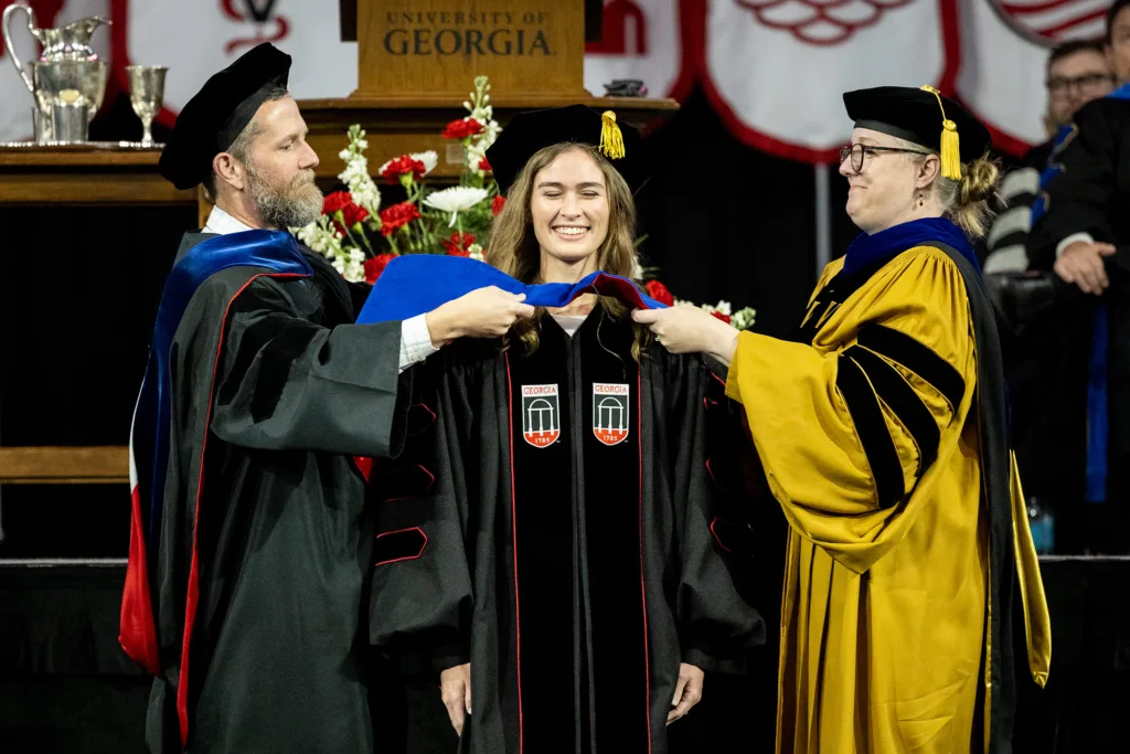 A graduate smiles while receiving their ceremonial hood at the fall graduate Commencement ceremony. (Billy Schuerman/UGA)