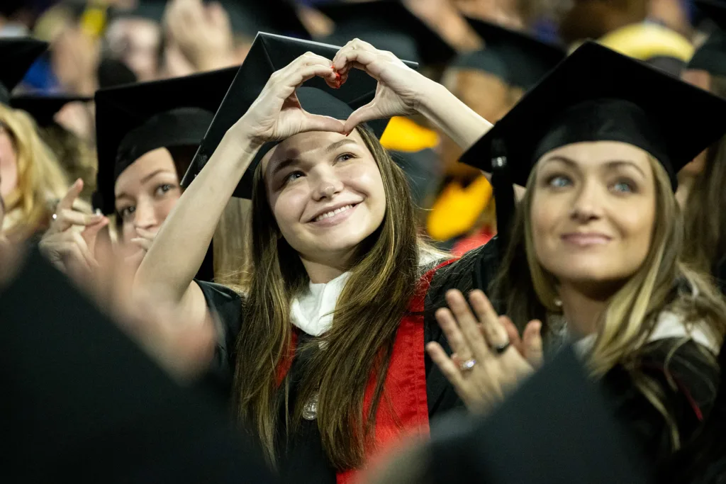 A graduate makes a heart to friends and family in the audience after the conferring of degrees at the fall graduate Commencement ceremony.