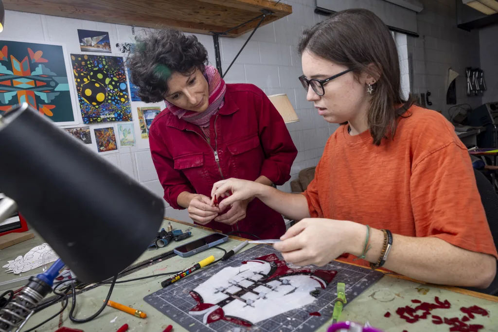 Two women work on a piece of stained glass art