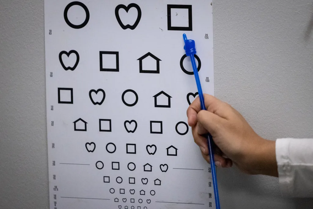 A medical student points to symbols on eye chart during a vision screening.