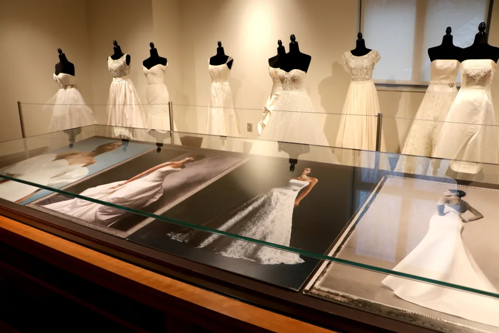 Glass display case showing photographs of Anne Barge bridal designs alongside mannequins dressed in white wedding gowns.