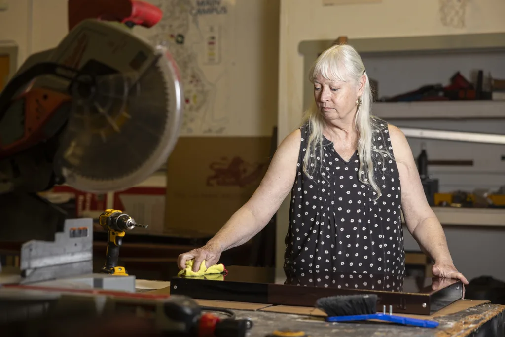 A woman runs a cloth over a sign in a workshop.