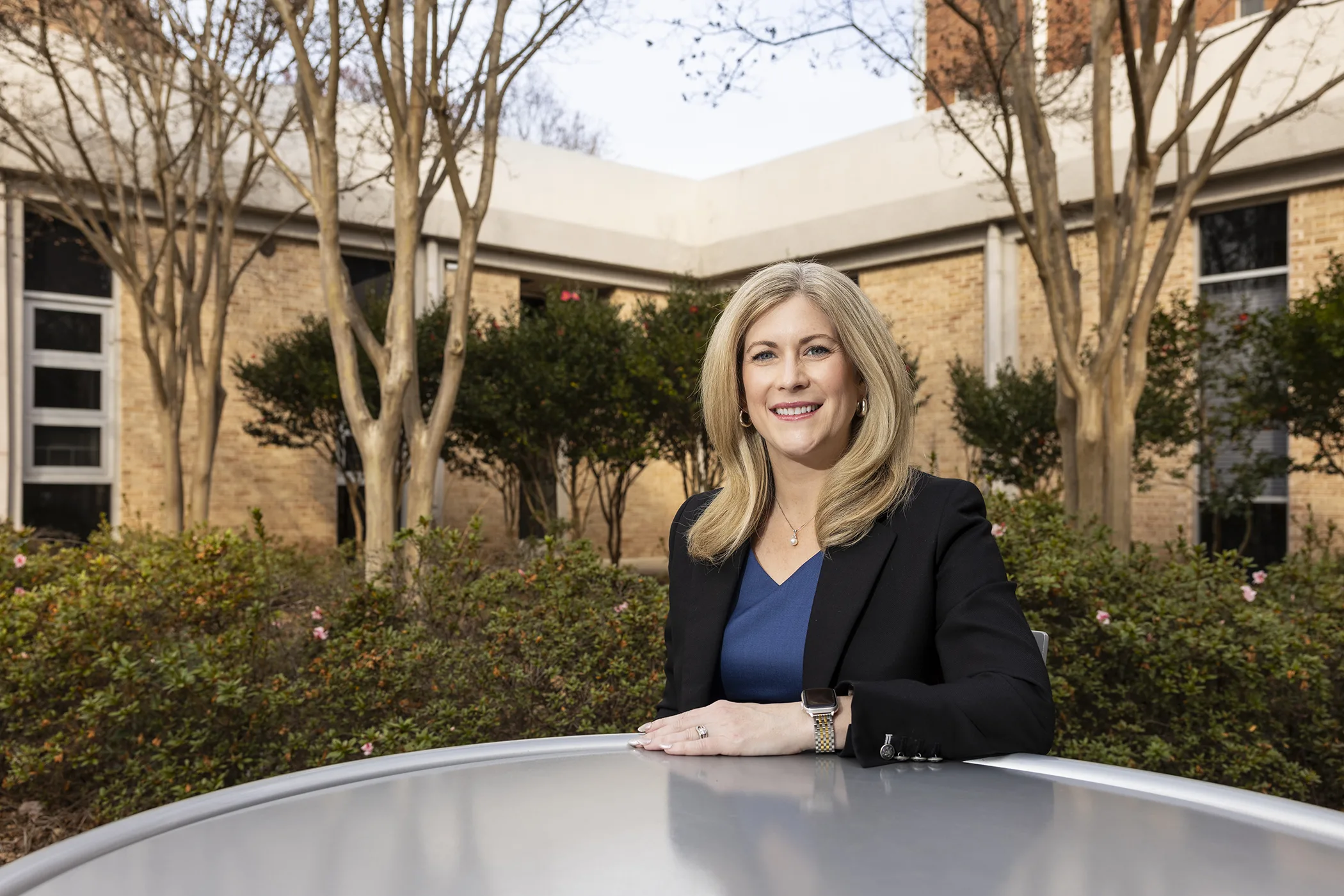 A woman sits outside, at a table, facing the camera