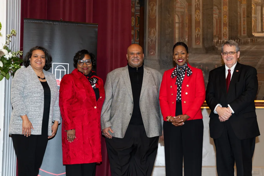 Five people stand together on stage in formal attire following lecture in the Chapel.
