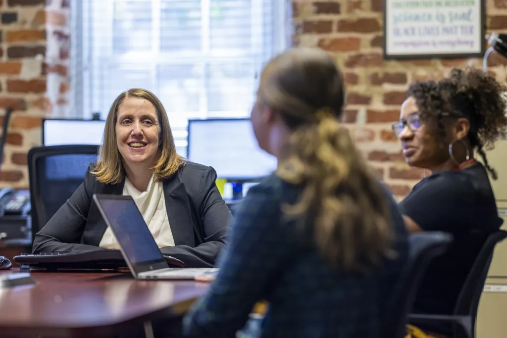 A woman sits at a table, talking with two younger women.
