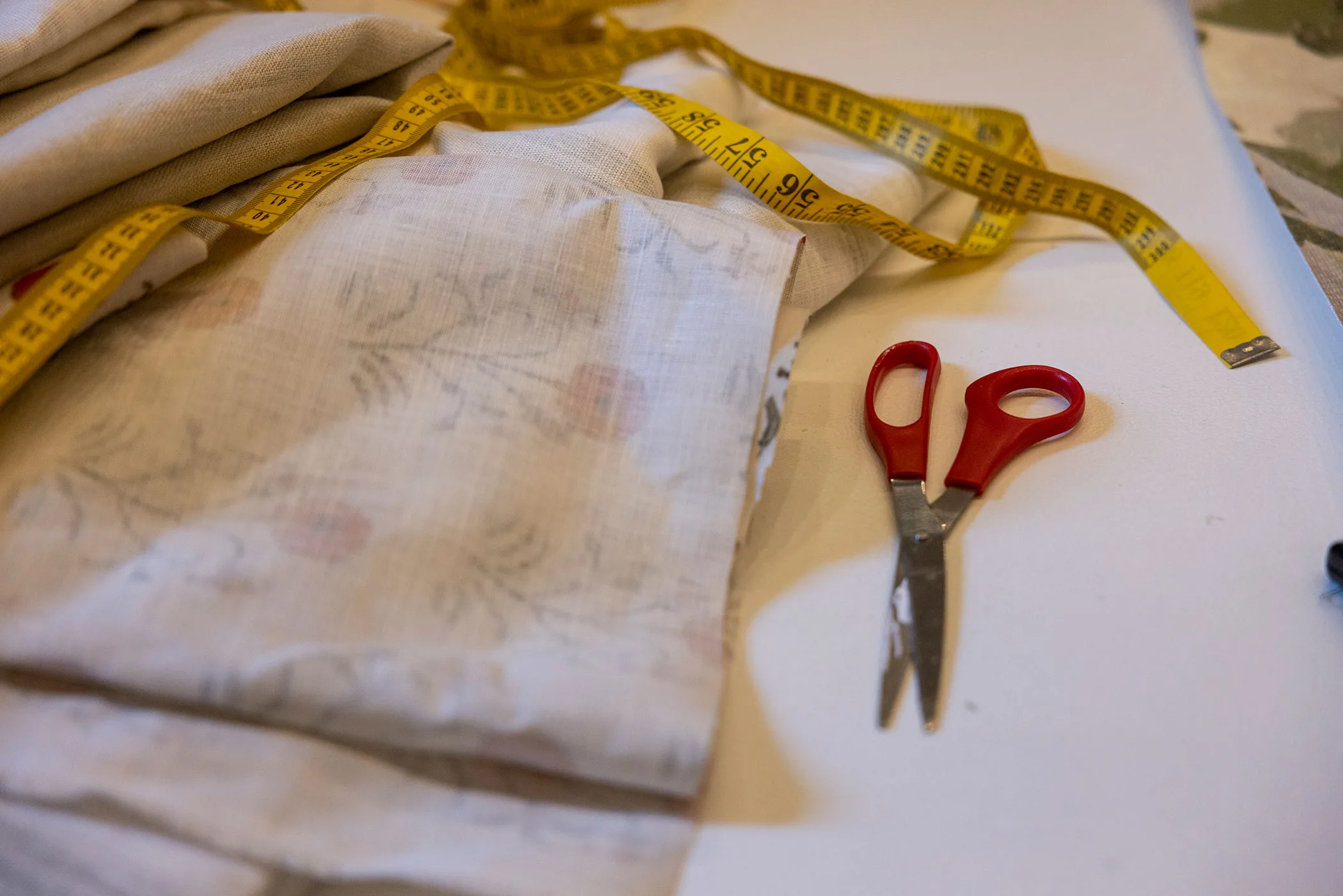Detail shot of fabric, a tape measure and scissors on a table.