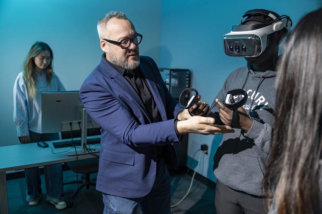 A professor and three students work with virtual reality equipment in a lab