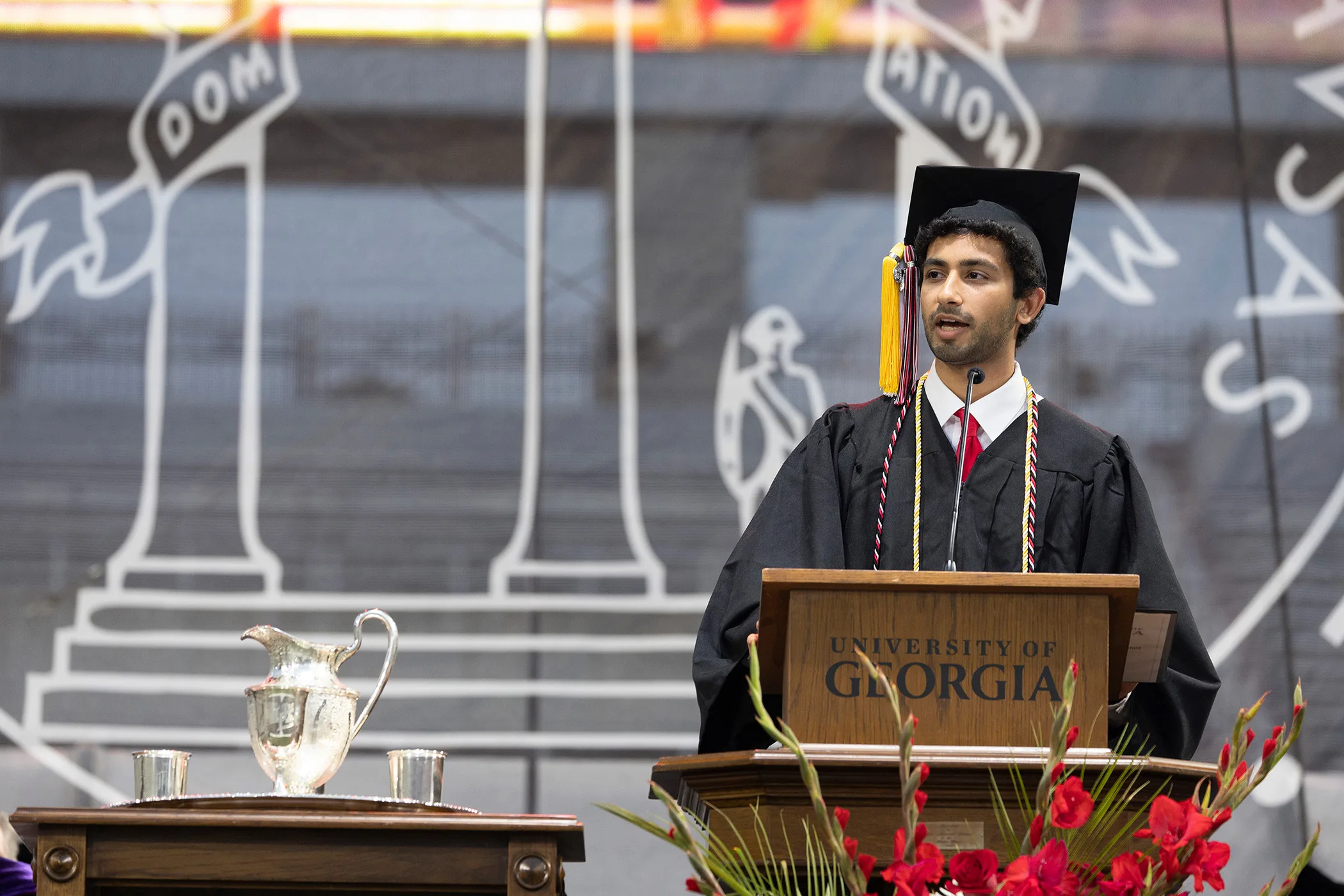 Sudhan Chitgopkar, wearing a graduation cap and gown, speaks at a podium during a UGA Commencement ceremony.