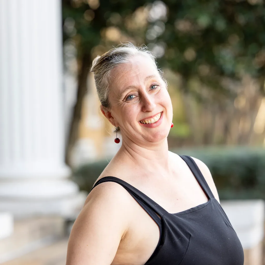A close up of a woman in a black, sleeveless top smiling outside.
