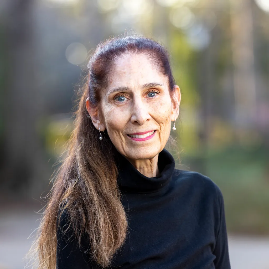 A closeup of a woman in a black turtleneck smiling outside.