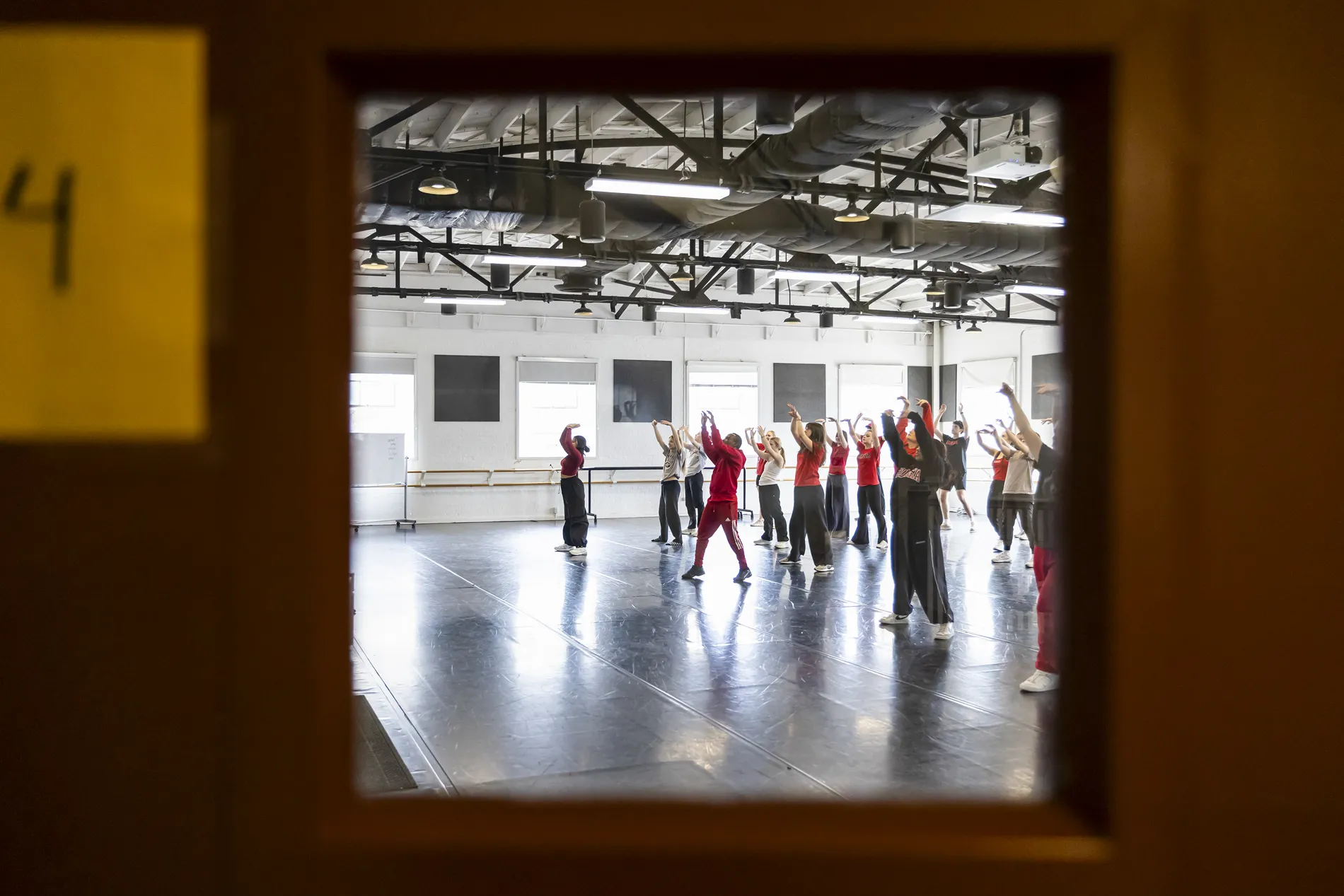 A view through a small square window of several dancers in a studio.